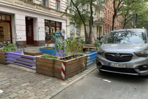 Hölzerne Stadtmöbel auf einem ehemaligen Parkplatz; davor in zweiter Reihe ein Auto